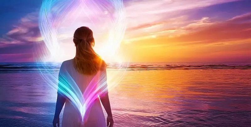 Eine Frau steht am Strand bei Sonnenuntergang, umgeben von leuchtenden Energiefeldern, die ihre spirituelle Bestimmung finden.