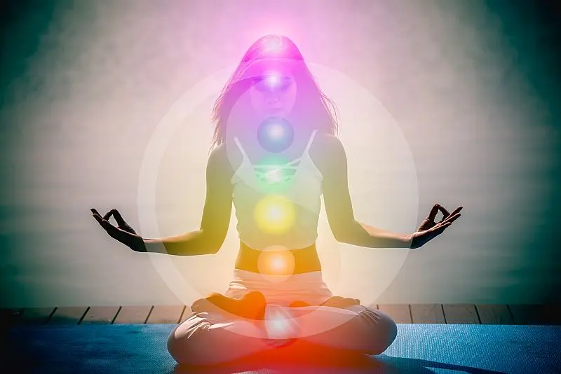 Eine Frau meditiert in Lotus-Position, umgeben von leuchtenden Chakren, während sie spirituelle Heilung erfährt.