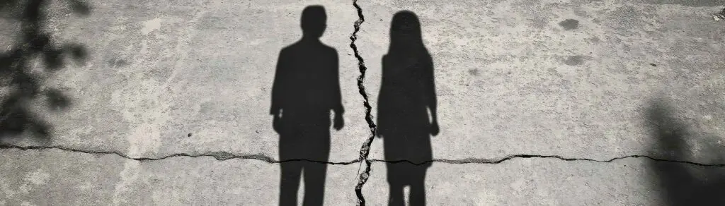 Zwei Schattensilhouetten stehen auf einer Straße, getrennt durch einen Riss, symbolisierend die Seelenpartner-Beziehung.