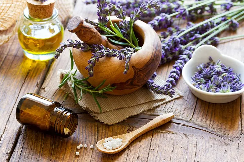Ein Holz-Mörser mit frischem Lavendel, homöopathische Globuli und ätherisches Öl symbolisieren die spirituelle Heilpraxis.