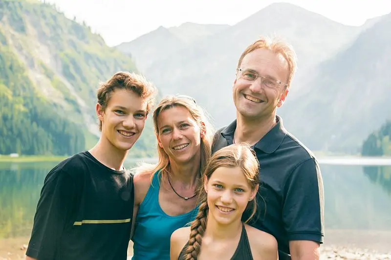 Eine lächelnde Familie steht vor einer malerischen Bergkulisse, symbolisiert durch die Seelenliebe und Harmonie.